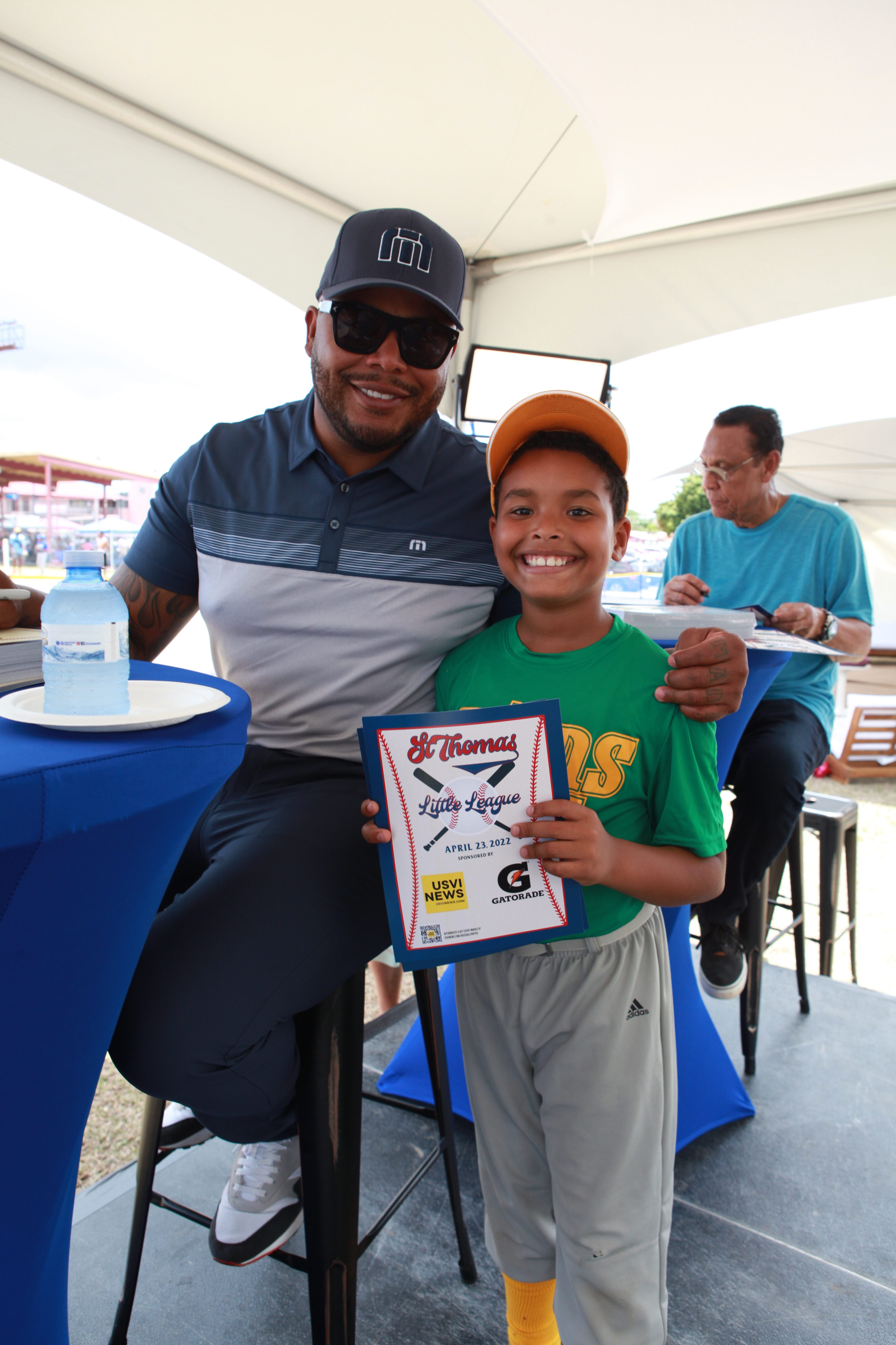 Tito Ortiz stands beside a young player during an autograph session on Little League opening day.