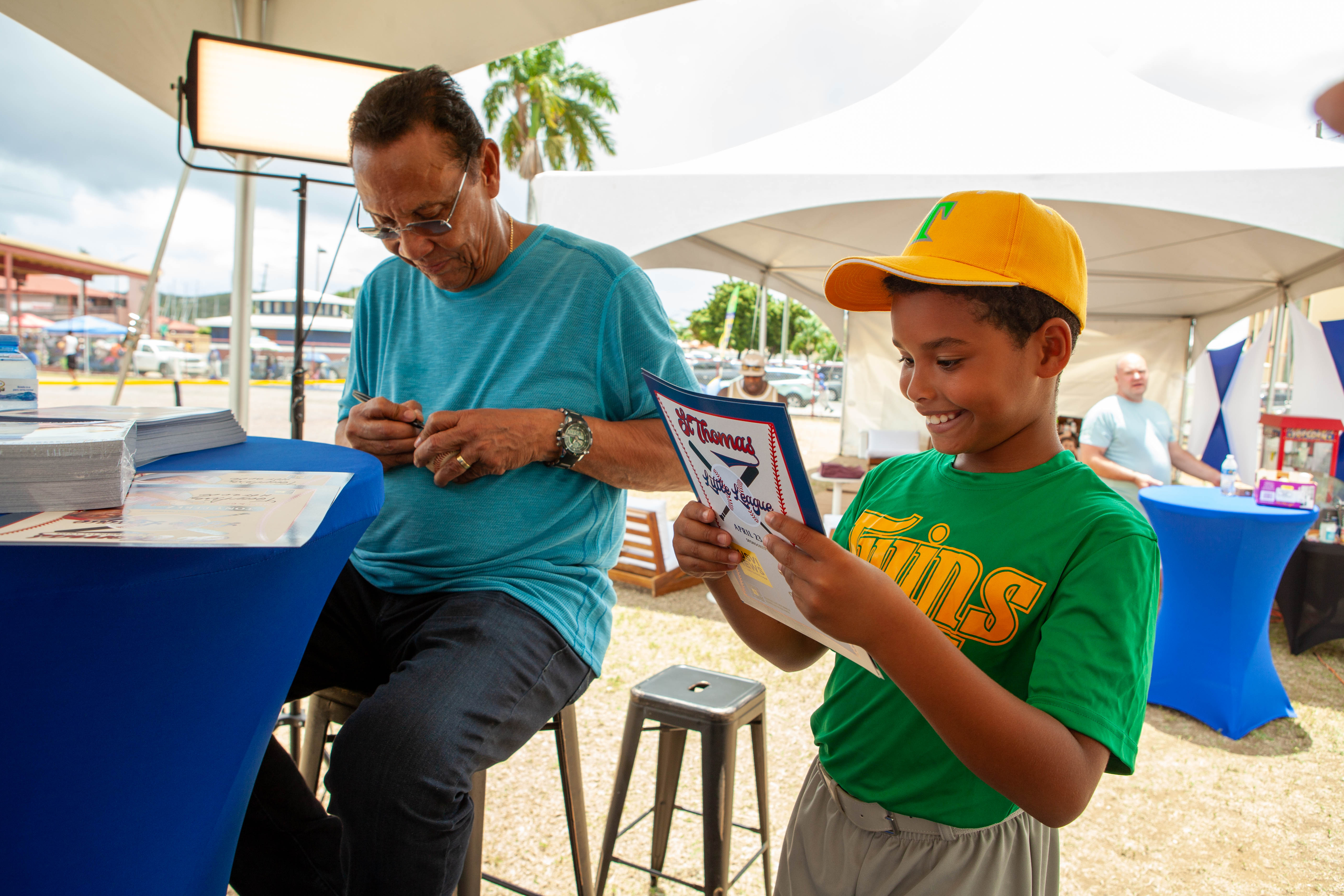 Tony Perez signs an item as a smiling boy holds a photo.