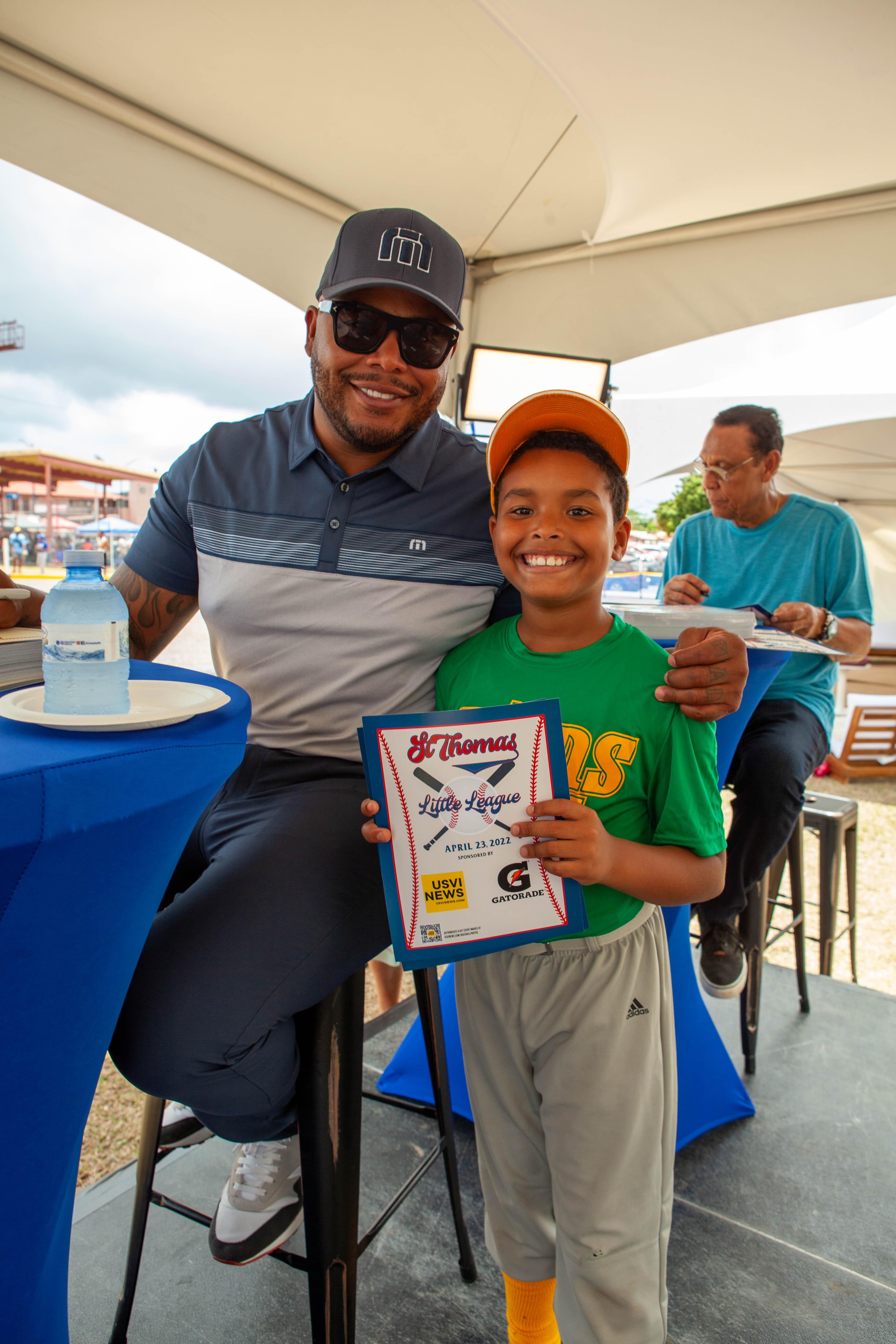 Andruw Jones poses with smiling boy holding framed certificate under tent.