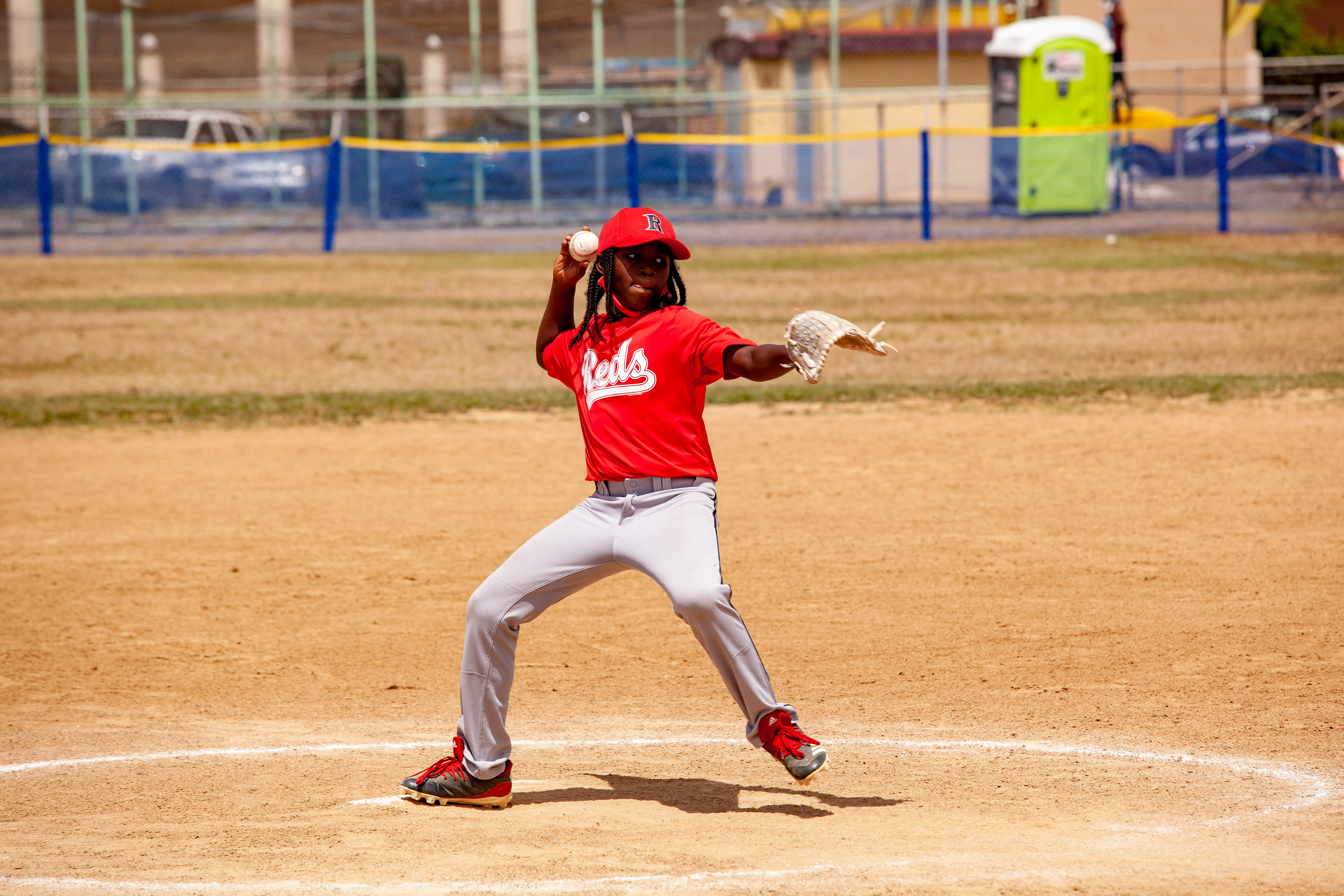 Youth pitcher in red uniform throws from the mound.