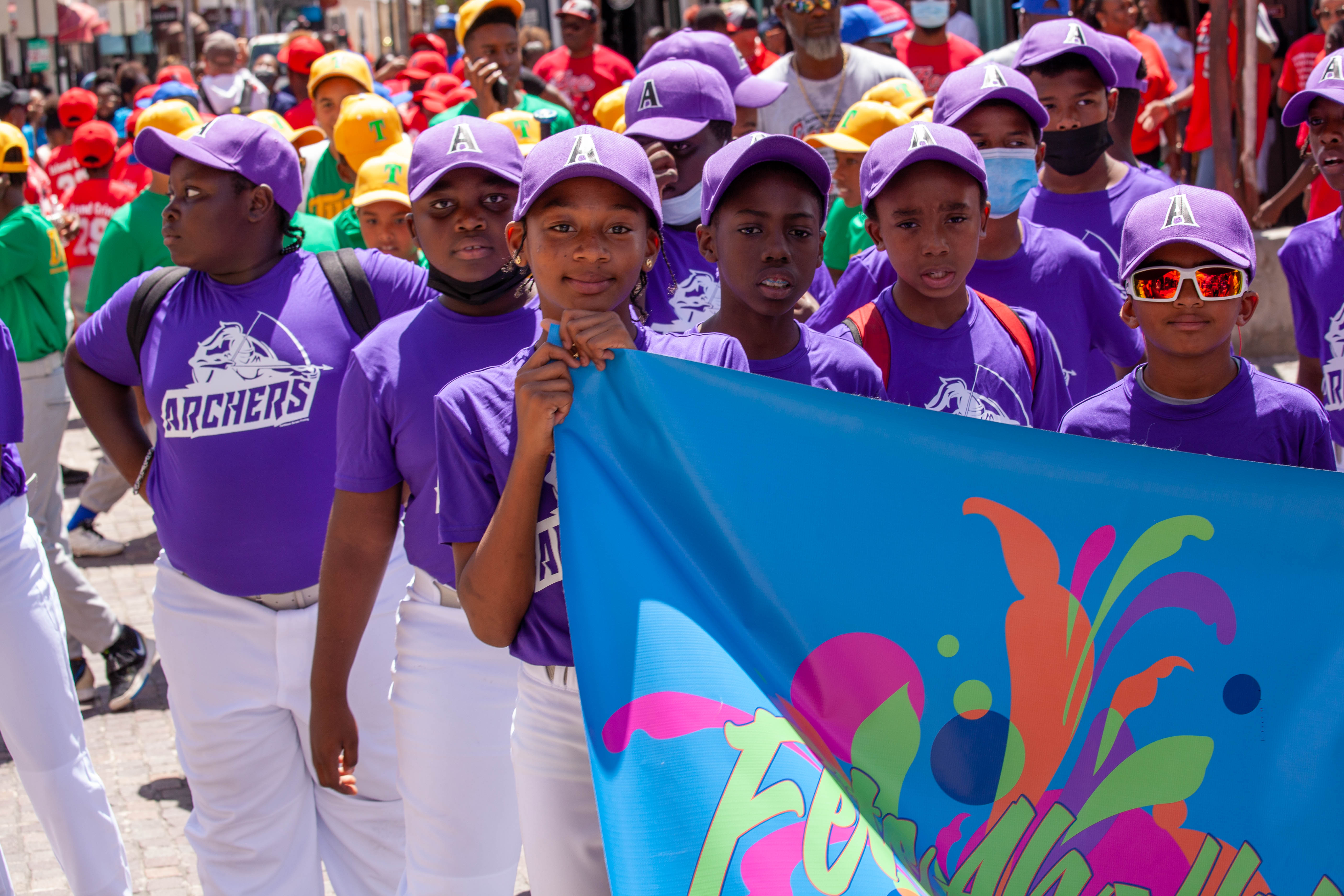 Purple-uniformed youth players carry a colorful banner in parade.